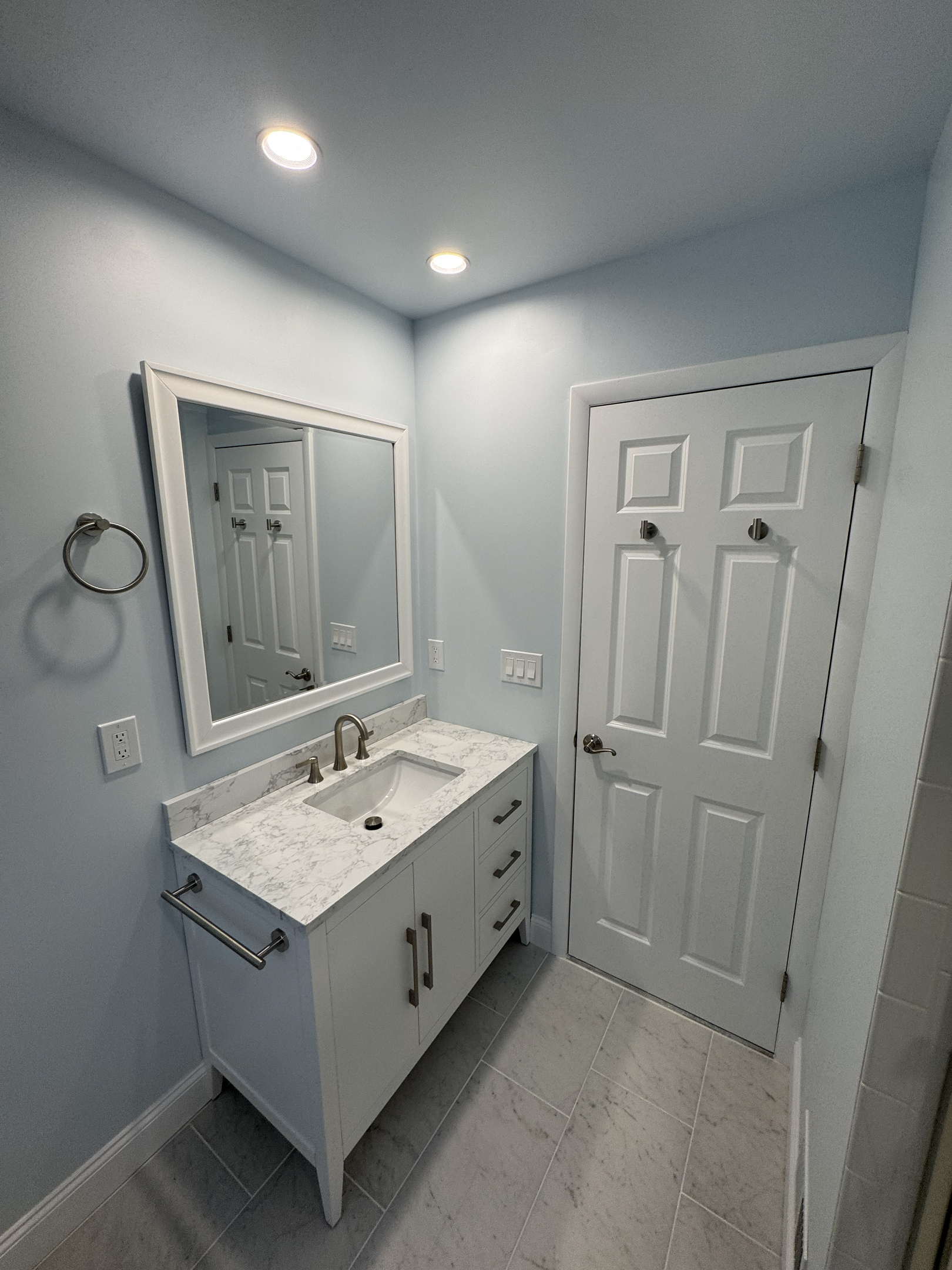 Modern gray bathroom with white vanity, marble countertop and adjacent closet door